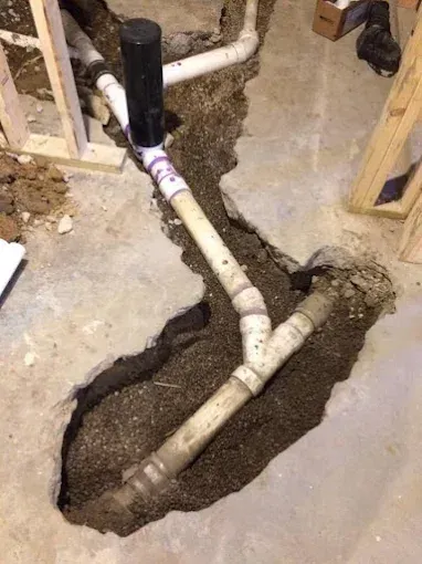 Exposed white PVC pipes in a rough concrete floor trench during plumbing work