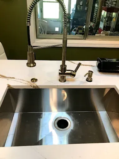 Kitchen sink with stainless steel basin, gooseneck faucet, and white countertop beside a window.