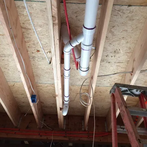 Ceiling under construction with exposed wooden beams and white PVC pipes
