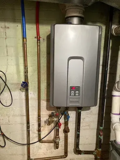 Wall-mounted gray tankless water heater with pipes and valves in a basement utility room