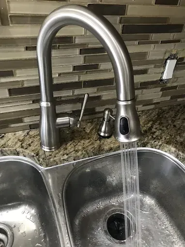 Kitchen faucet running water into a stainless-steel sink set against a tile backsplash