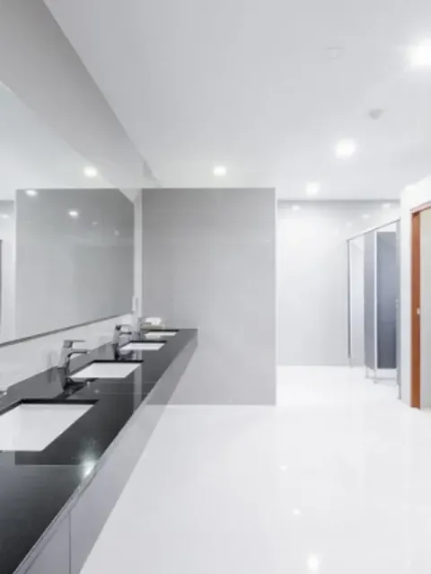 Modern white bathroom with a long black countertop, sinks, mirrors, and a glass shower area.