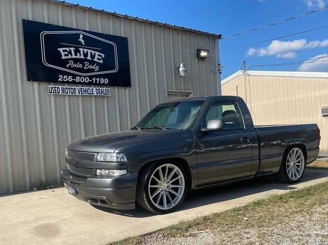 Dark gray custom pickup truck parked outside Elite Trucks shop under a blue sky.