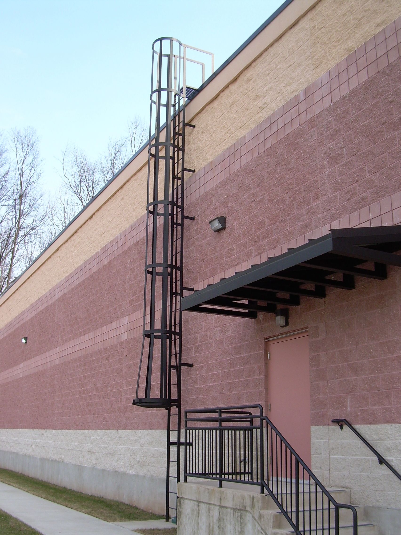 Pink brick building exterior with a black metal fire escape and stairs against a pale sky