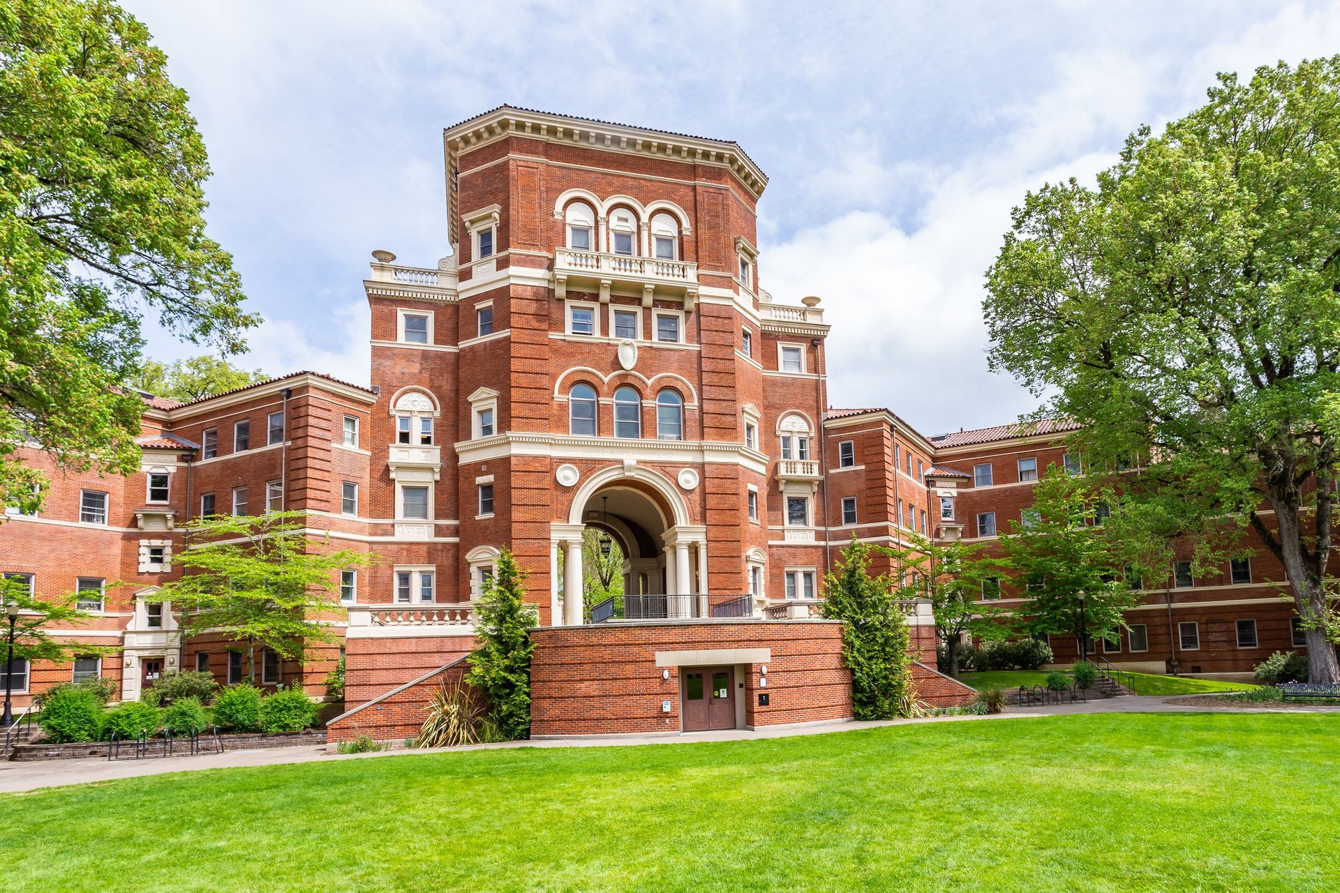 A large brick building with a tower on top of it is surrounded by trees and grass.