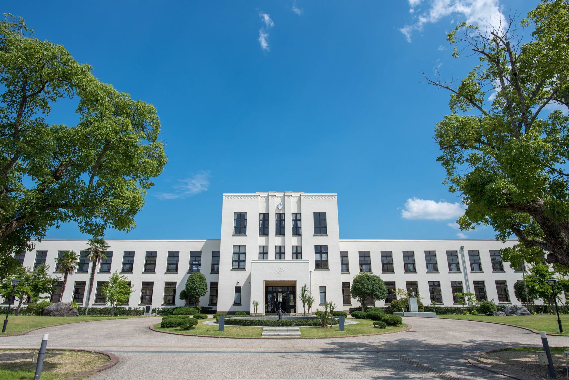 A large white building with trees in front of it and a blue sky in the background.