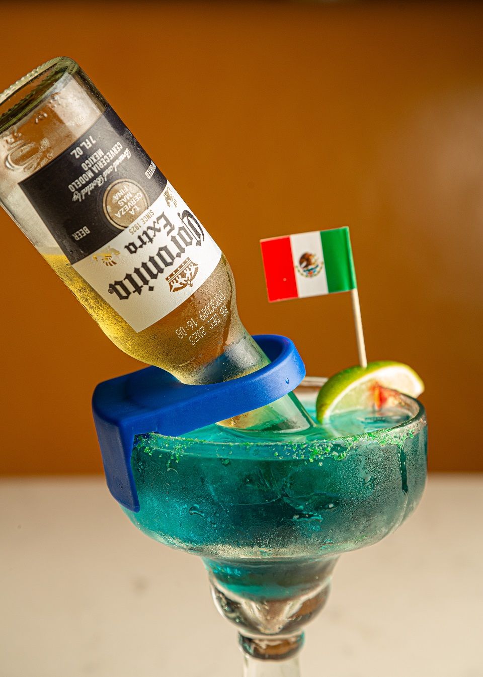 A bottle of corona extra is being poured into a margarita glass