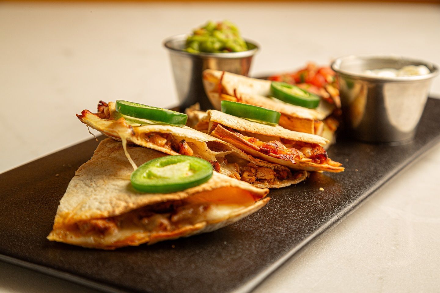 A tray of quesadillas with guacamole and sour cream on a table.
