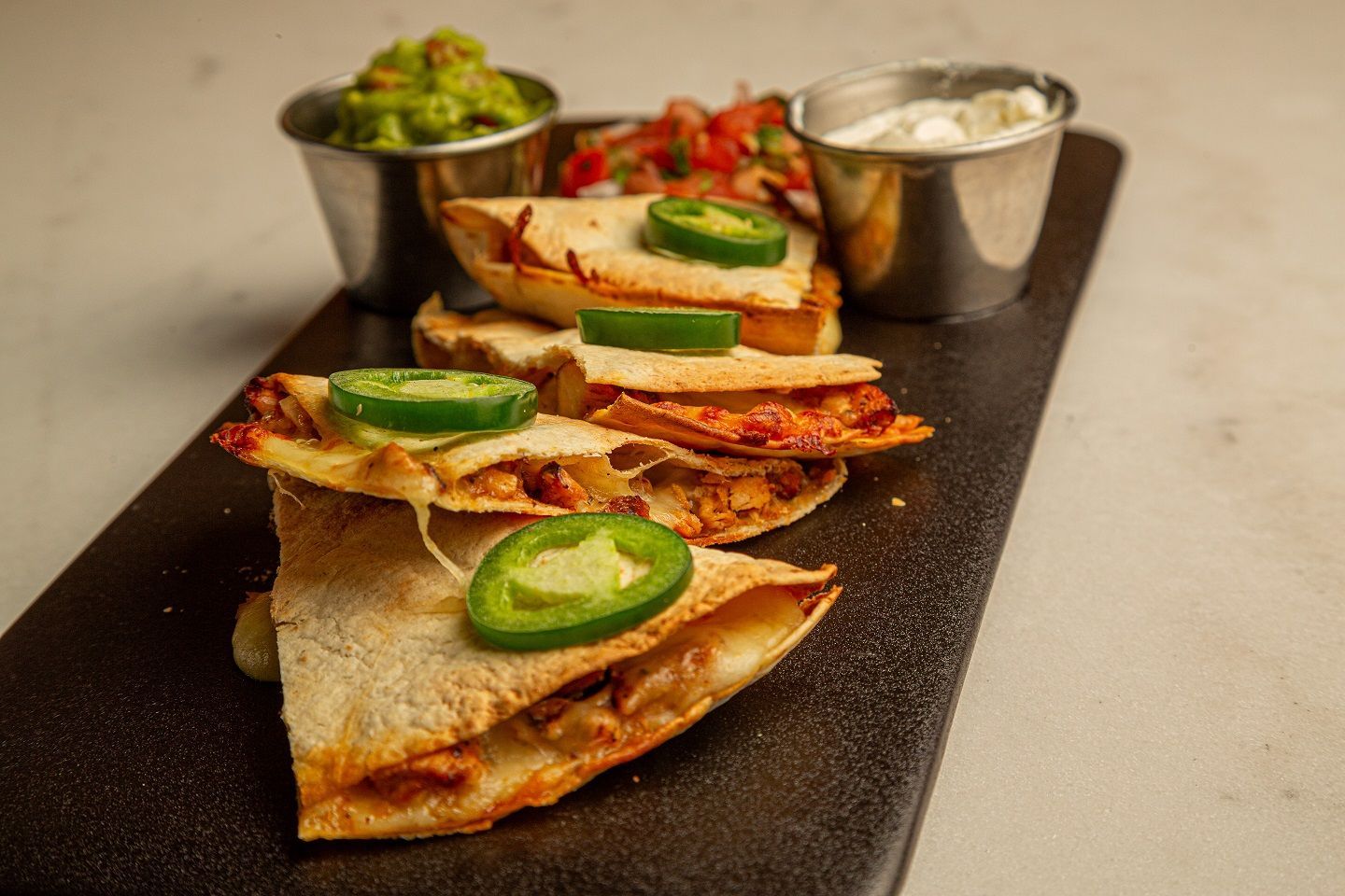 A tray of quesadillas with jalapenos and guacamole on a table.