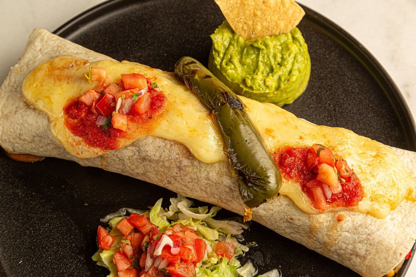 A burrito with guacamole and salsa on a black plate.
