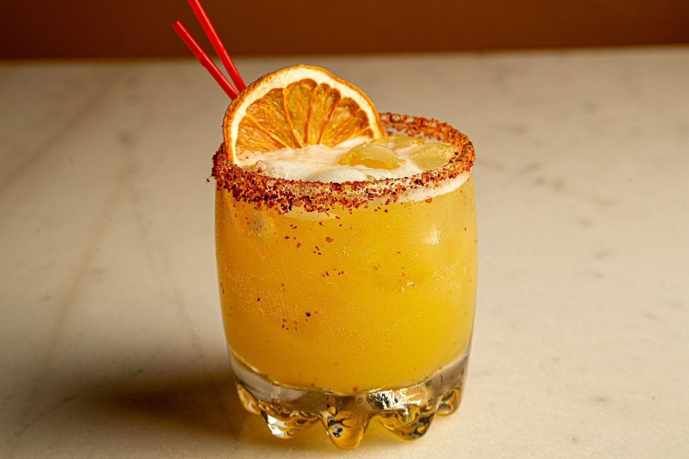 A close up of a margarita with an orange slice on top on a table.