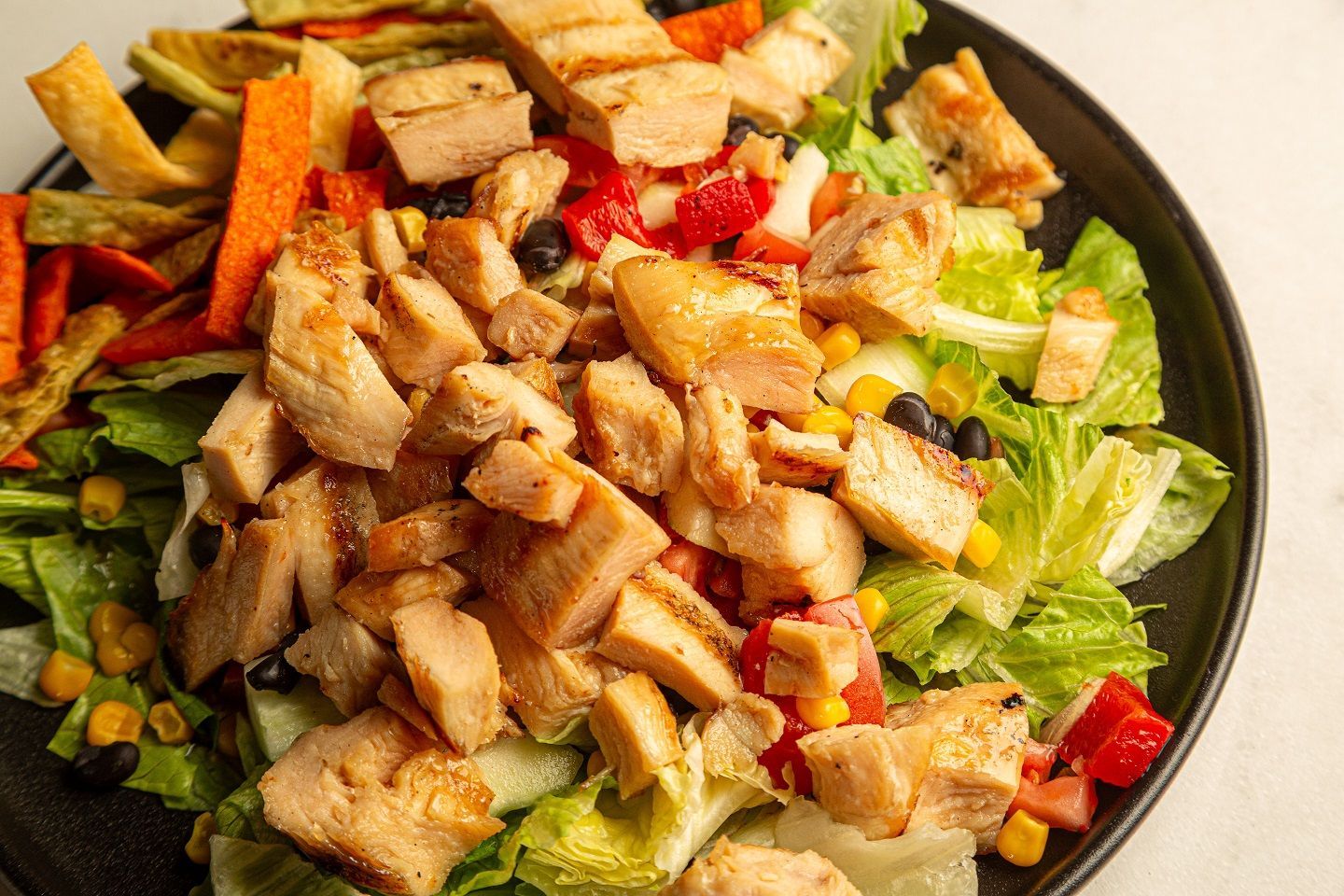 A close up of a salad with chicken and vegetables on a plate.