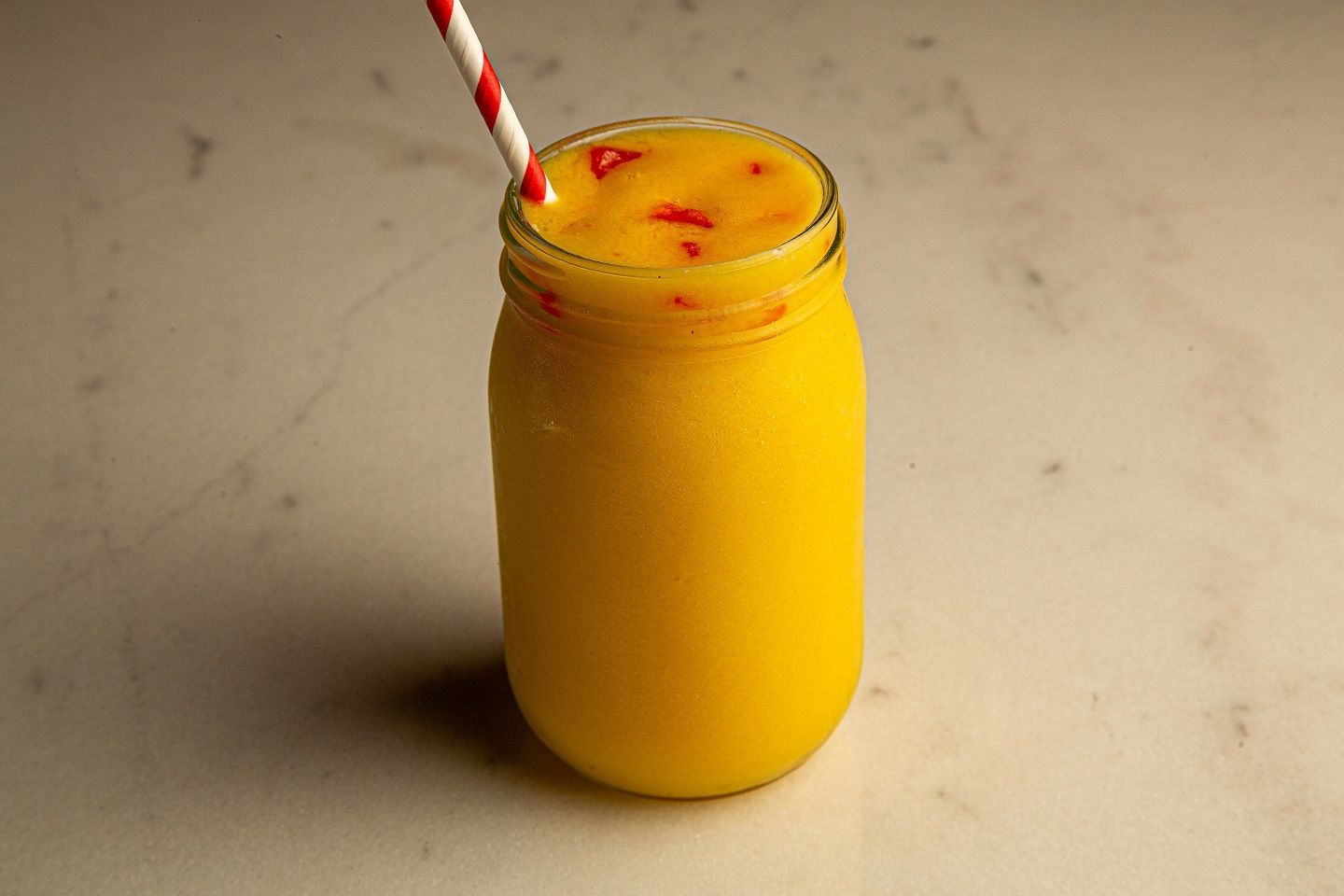 A yellow smoothie in a mason jar with a red and white straw.