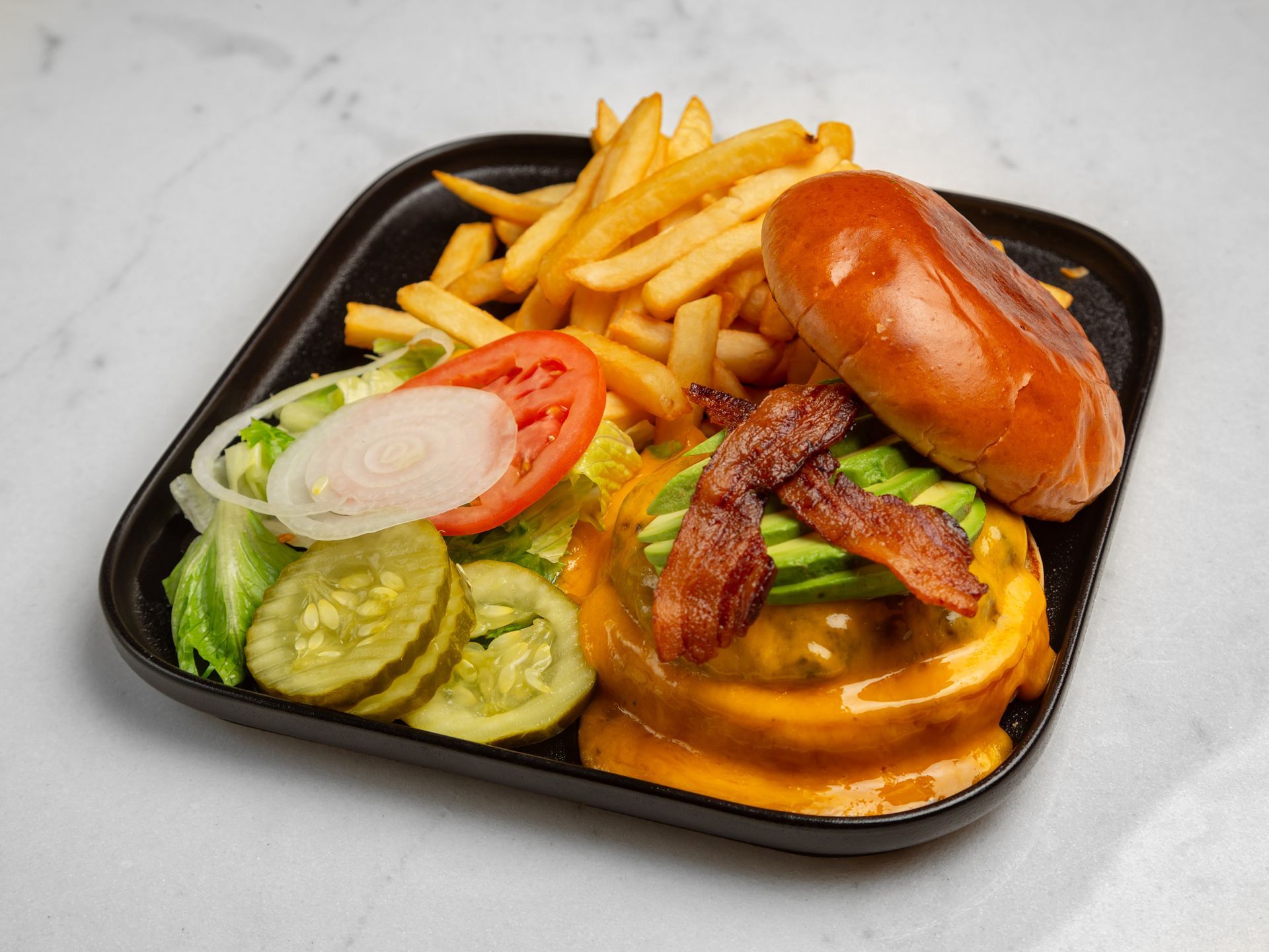 A hamburger and french fries on a black plate on a table.