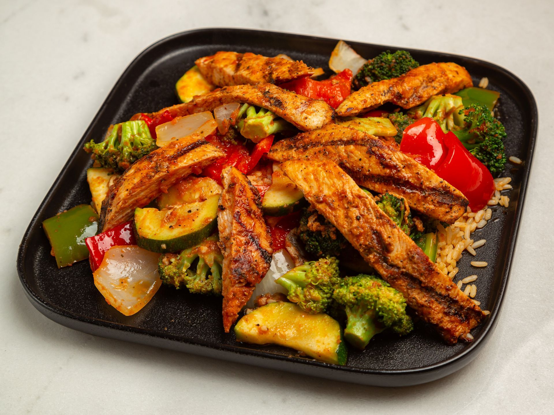 A black plate topped with chicken and vegetables on a table.