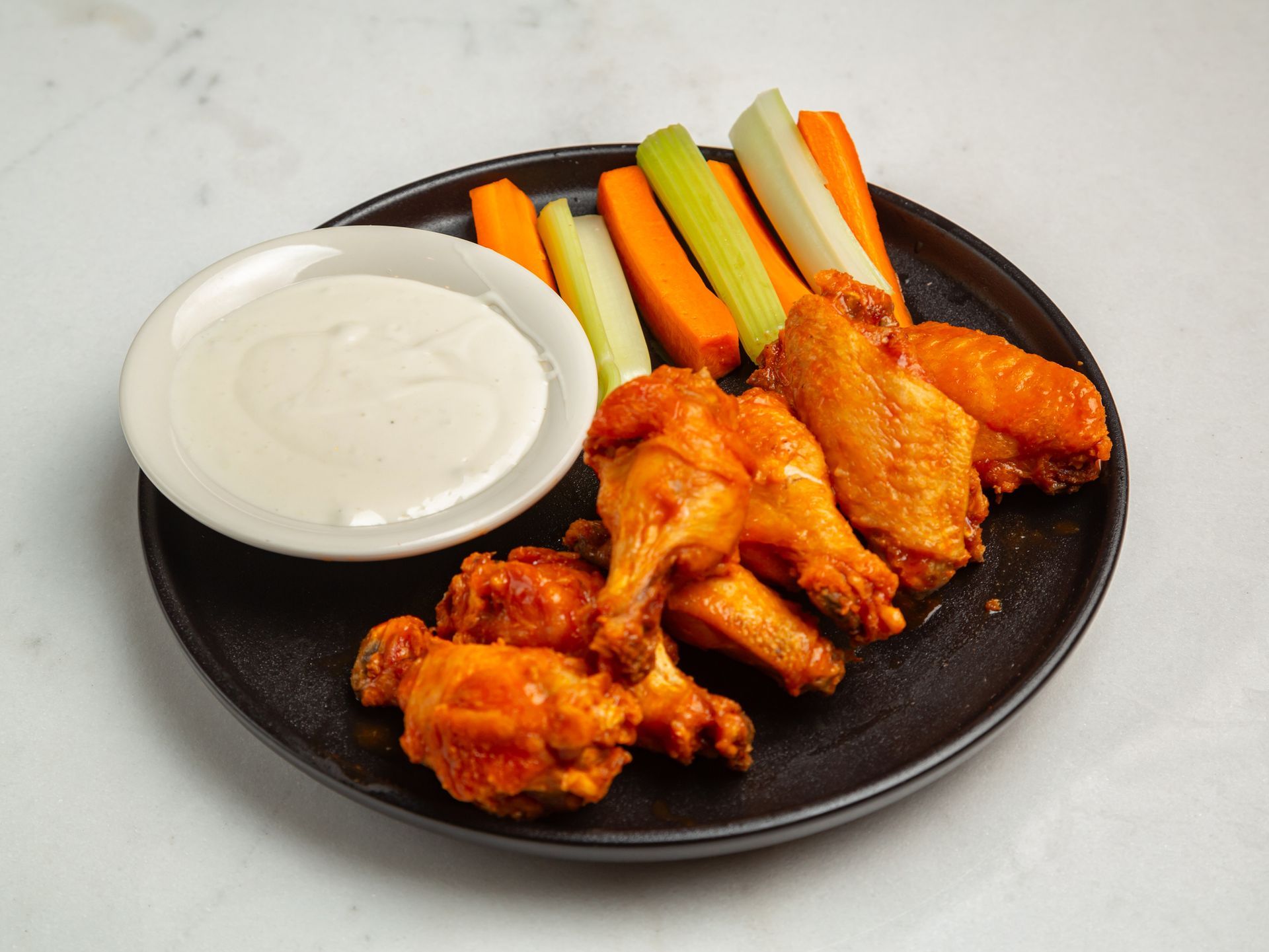 A black plate topped with chicken wings , carrots , celery and ranch dressing.