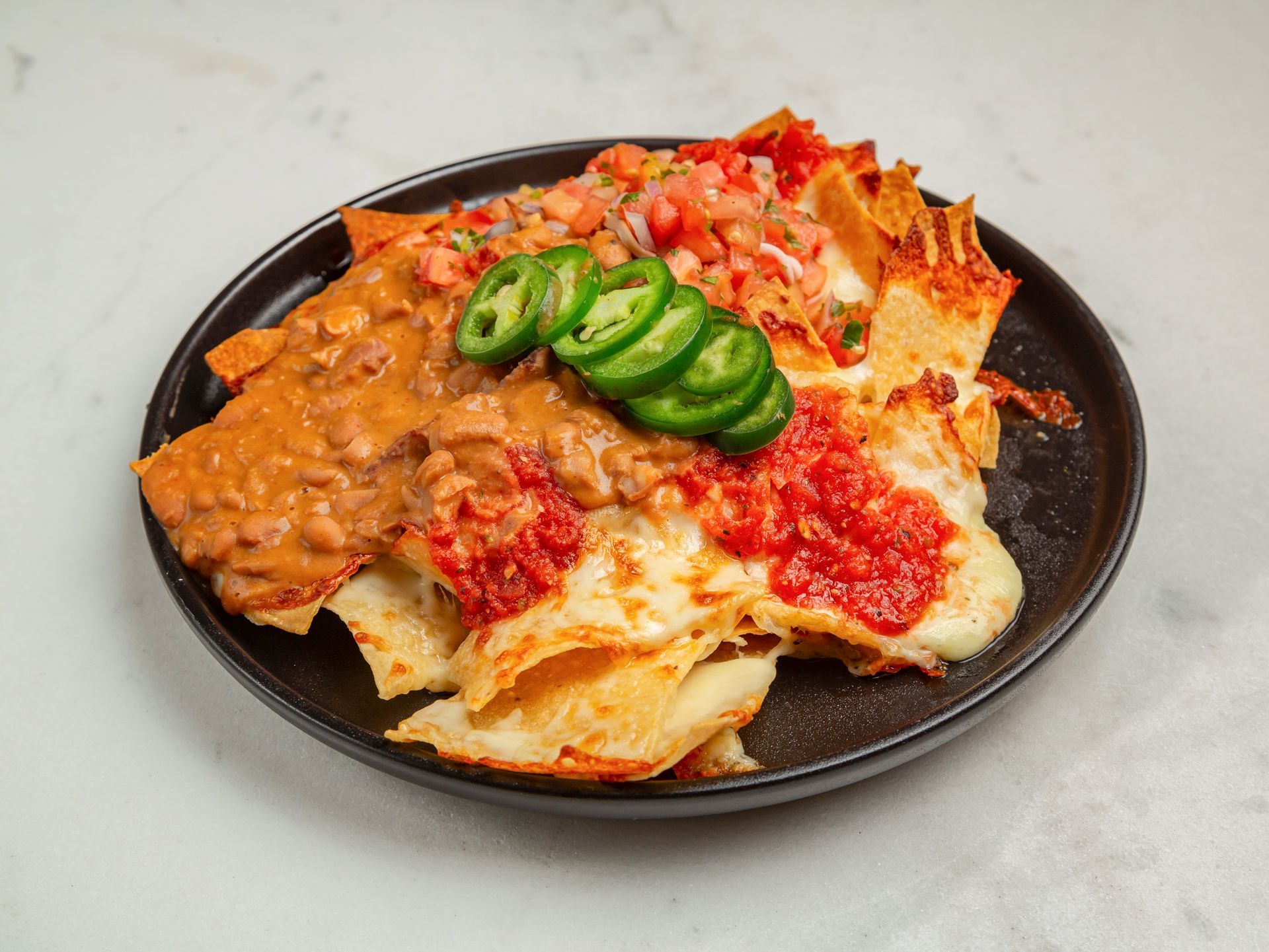 A plate of nachos with beans , cheese , salsa and jalapenos on a table.