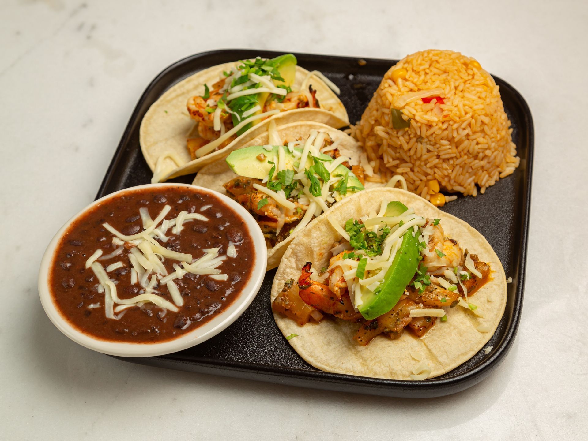 A tray of tacos , rice and beans on a table.