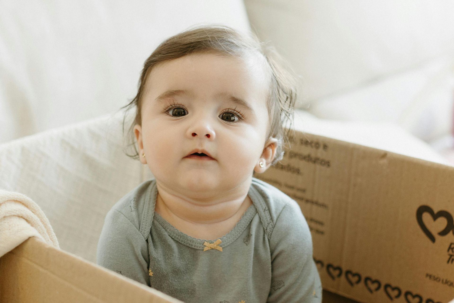 A child is sitting in a cardboard box looking at the camer.
