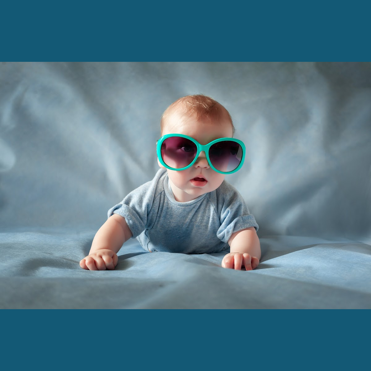 A baby wearing sunglasses is crawling on a bed