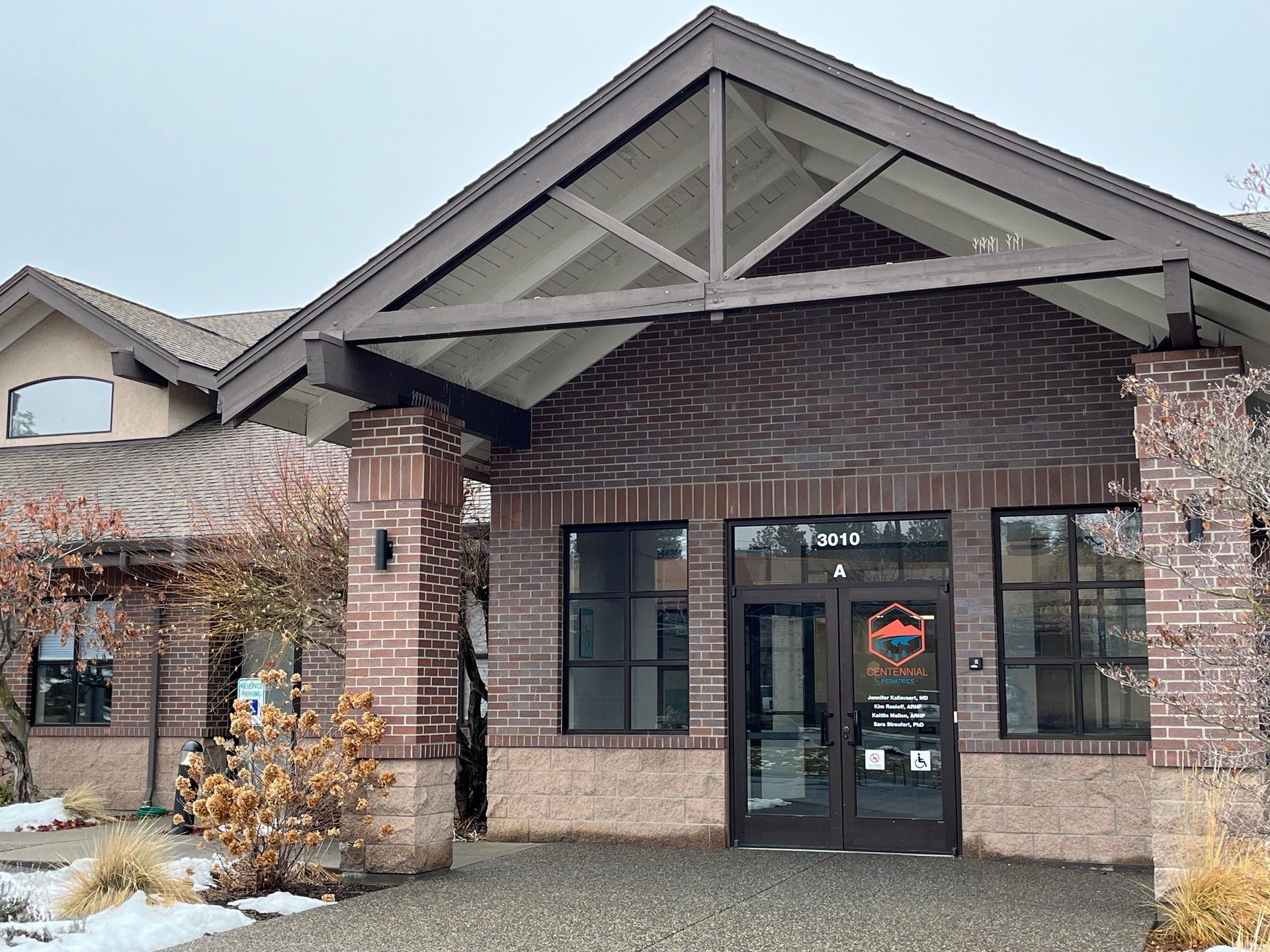 Brick building with a dark roof and entrance, featuring glass doors and windows; small snow on the ground.