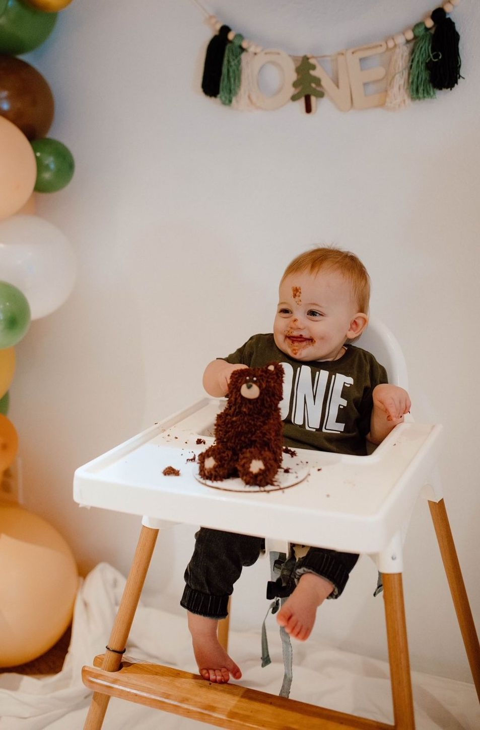 A baby is sitting in a high chair eating a cake.
