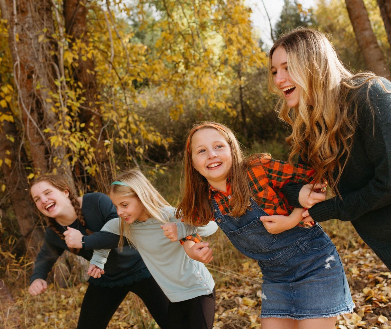 Four smiling people running in a forest with autumn leaves.