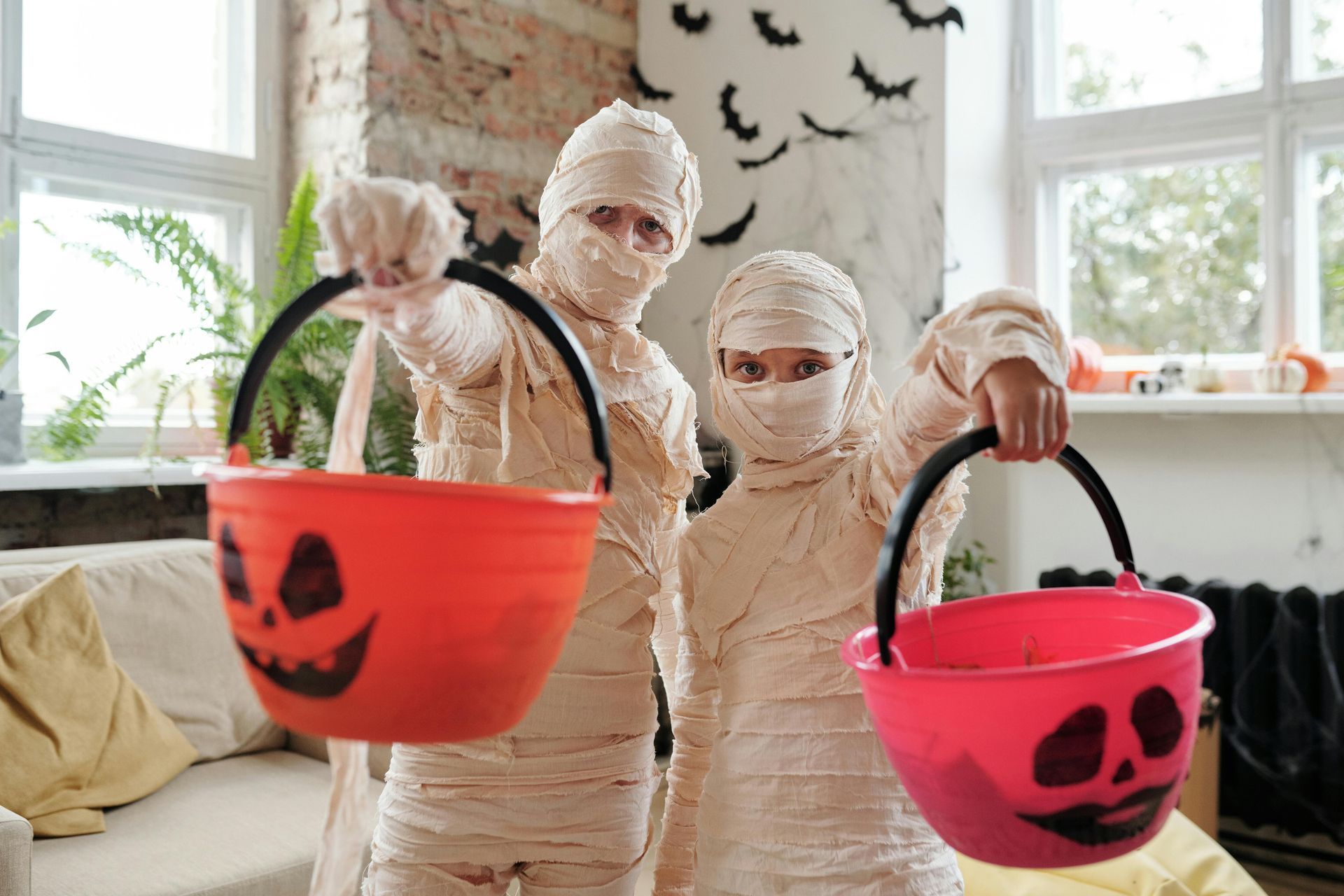 Two children dressed as mummys are holding buckets of halloween treats.
