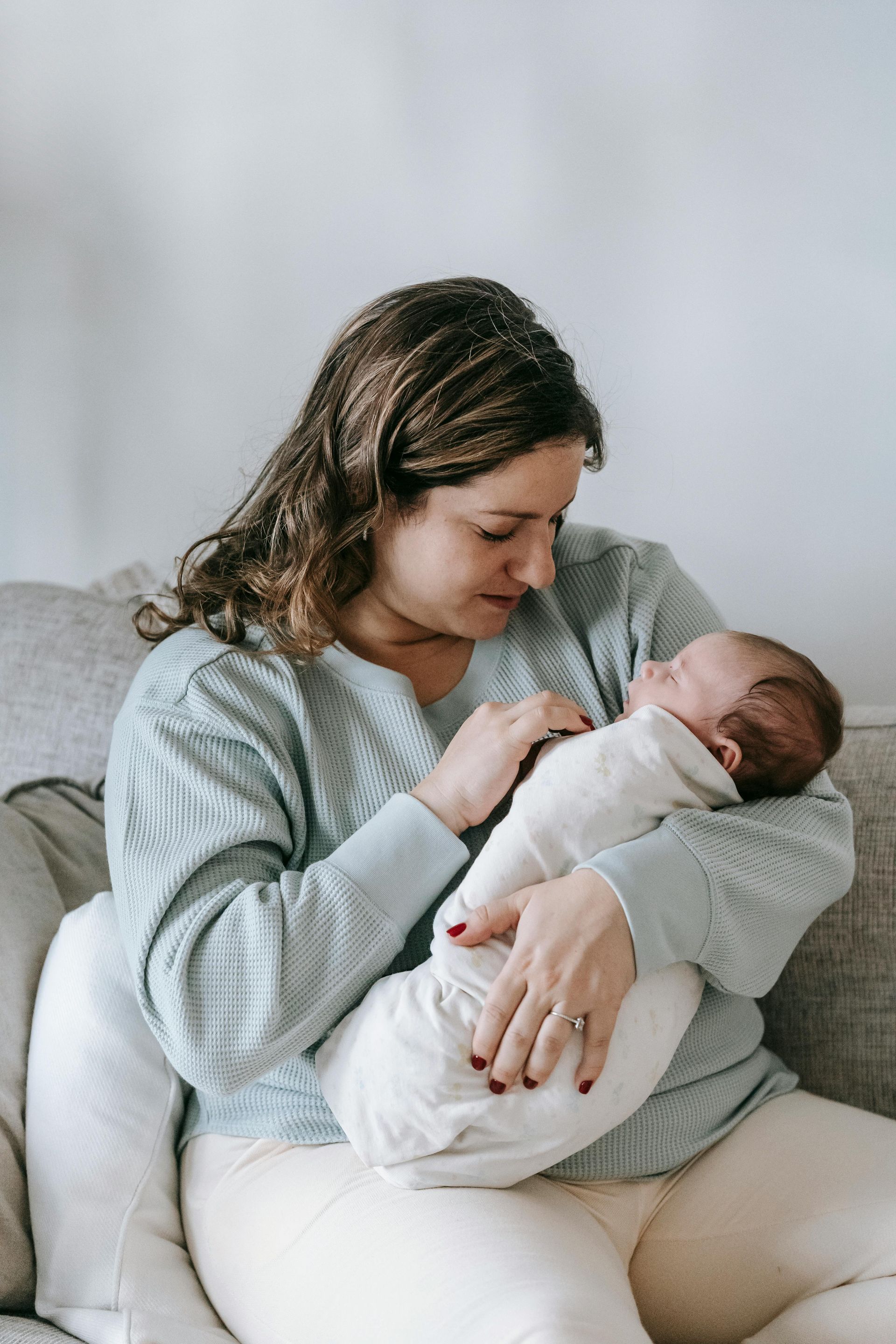 A woman is holding a baby in her arms while sitting on a couch.
