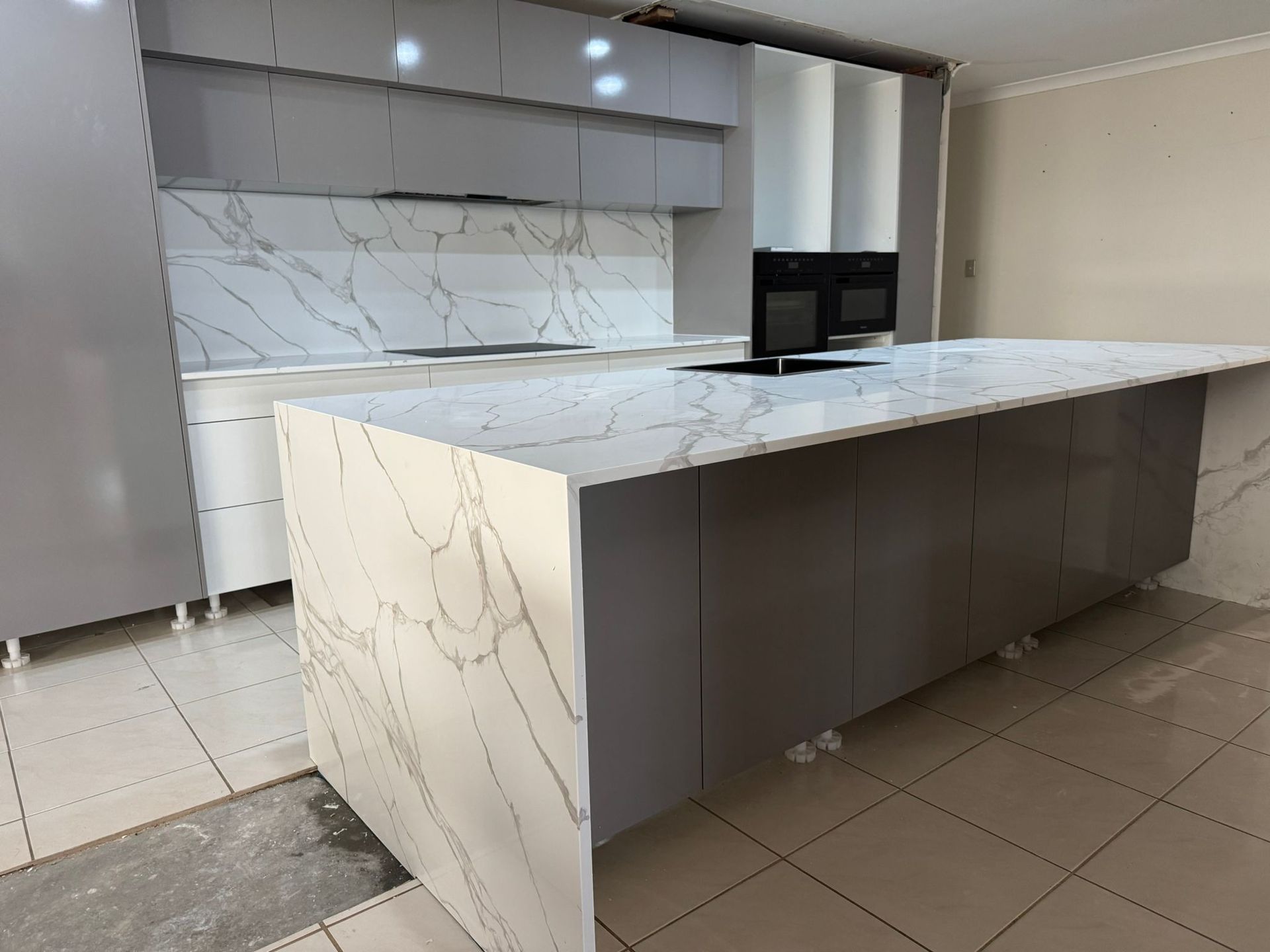 Modern kitchen with large marble island, gray cabinets, and built-in oven.