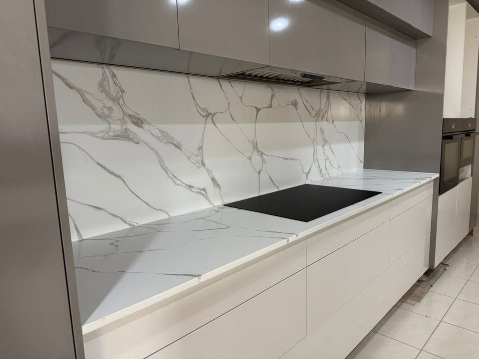 Modern kitchen with white cabinets, marble-look backsplash, and a black cooktop on a long counter