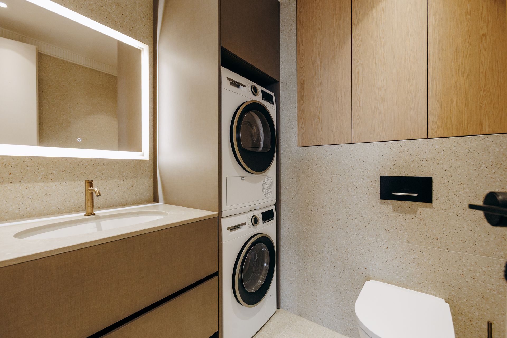 Modern laundry room with stacked washer and dryer, vanity sink, mirror, and beige cabinets