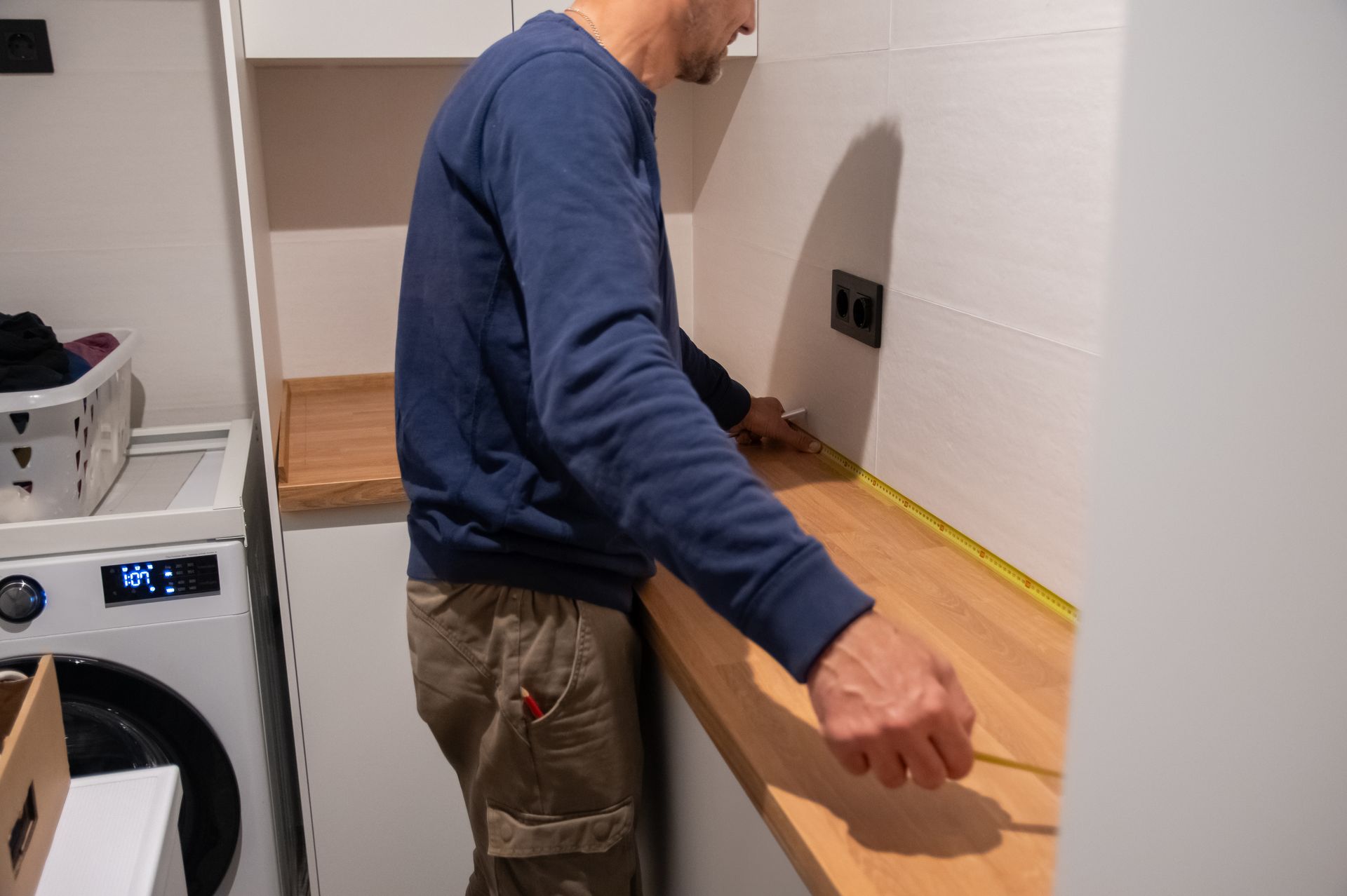 Person installing a wooden countertop in a small kitchen with a washing machine nearby