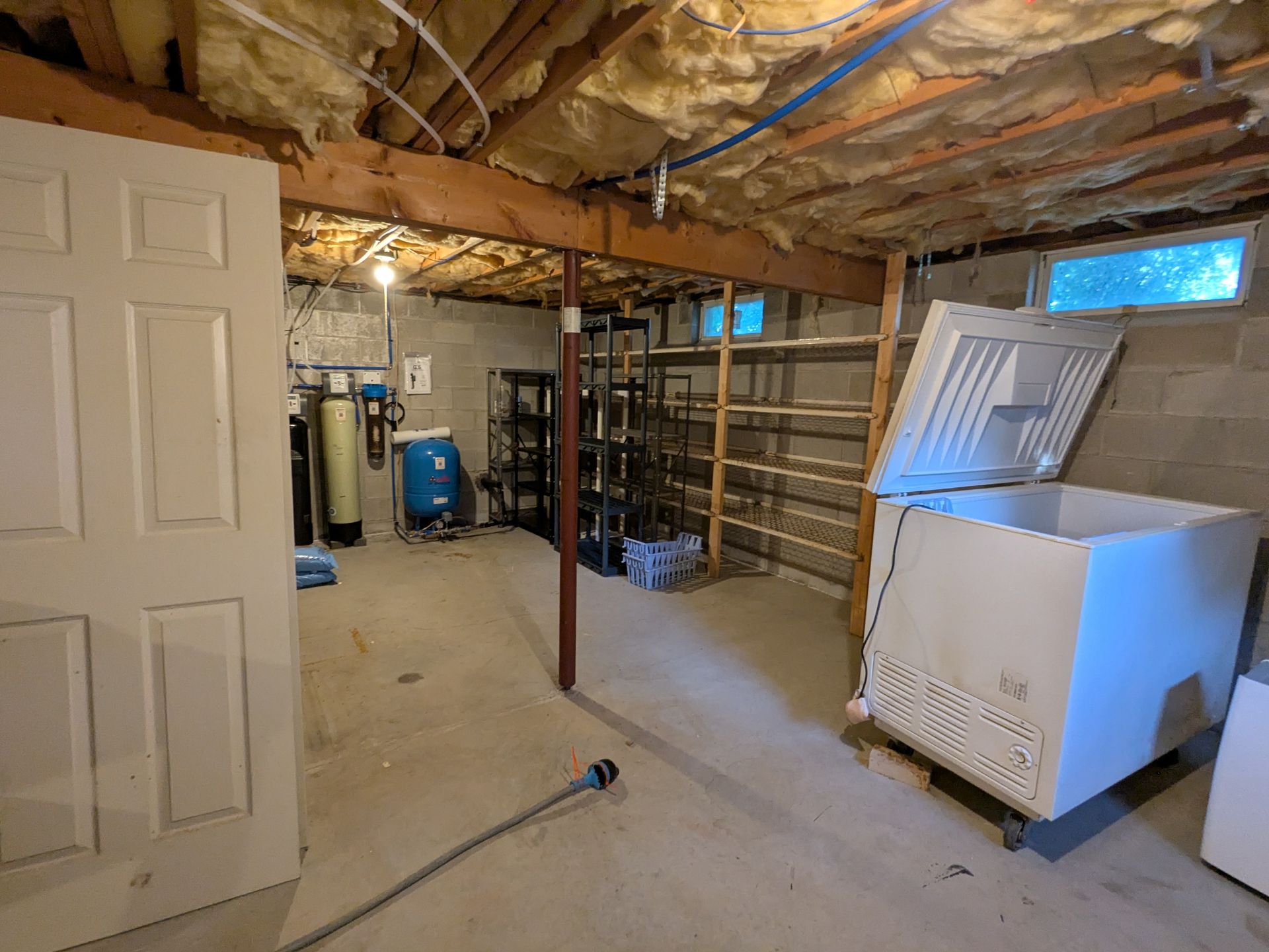 Unfinished basement with exposed insulation, water heater, shelves, and a washer and dryer.