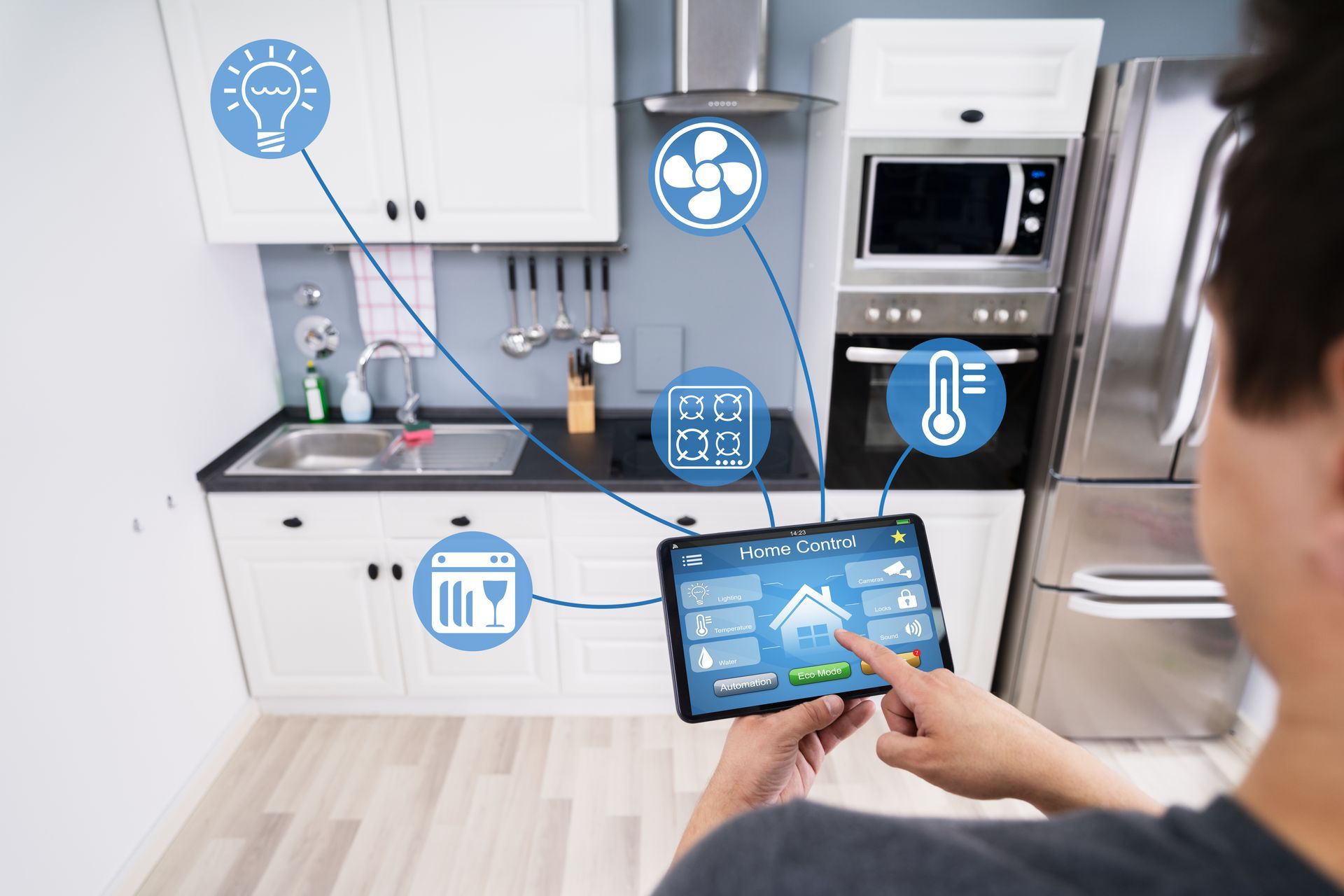Person uses a tablet to control smart kitchen appliances with digital icons above the counters.