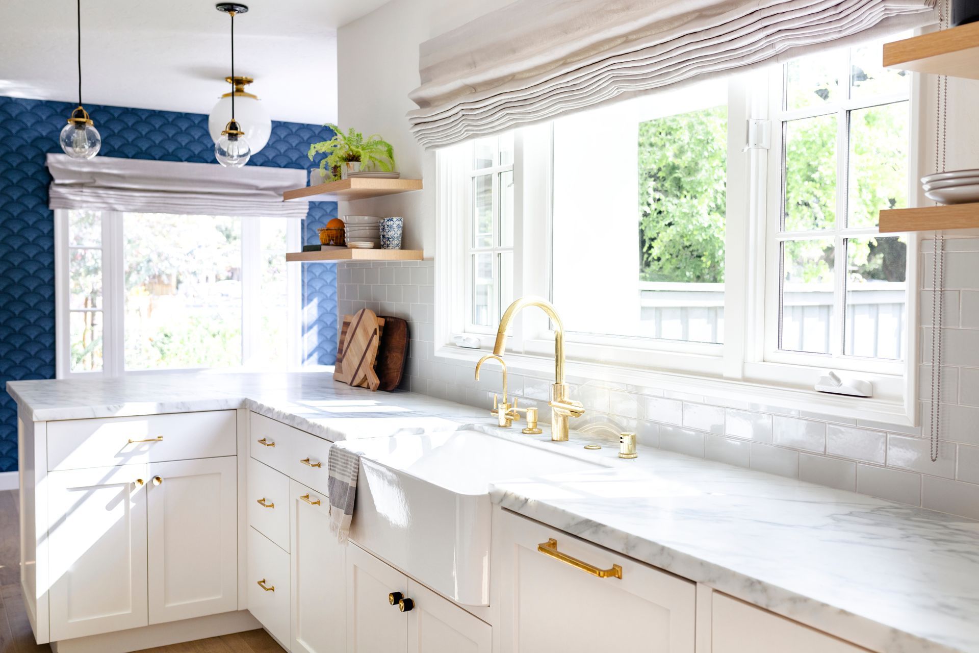 Bright white kitchen with gold fixtures, marble countertops, and a large window over the sink