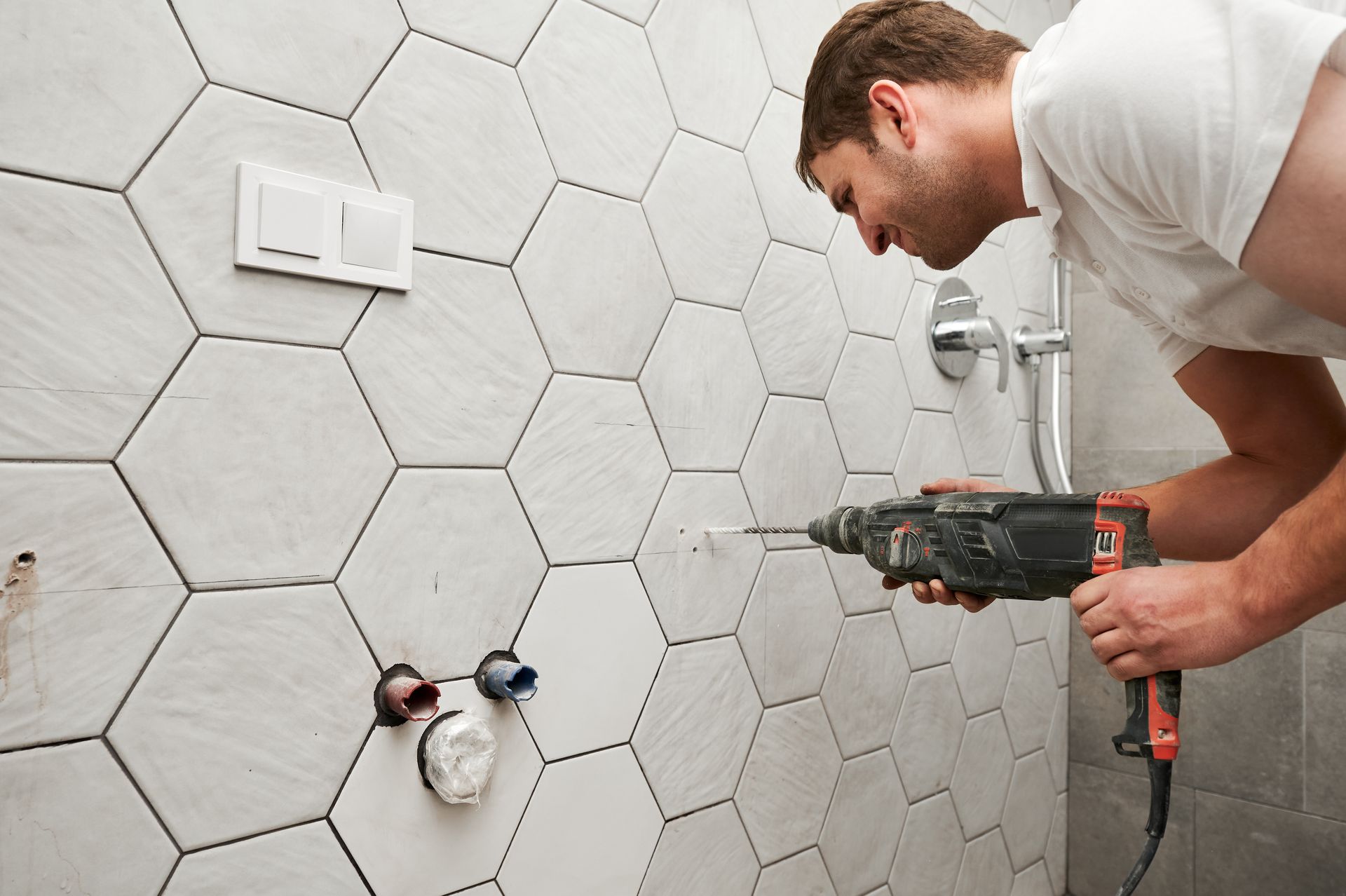 Man drilling hexagon tile on a bathroom wall, installing plumbing fixture