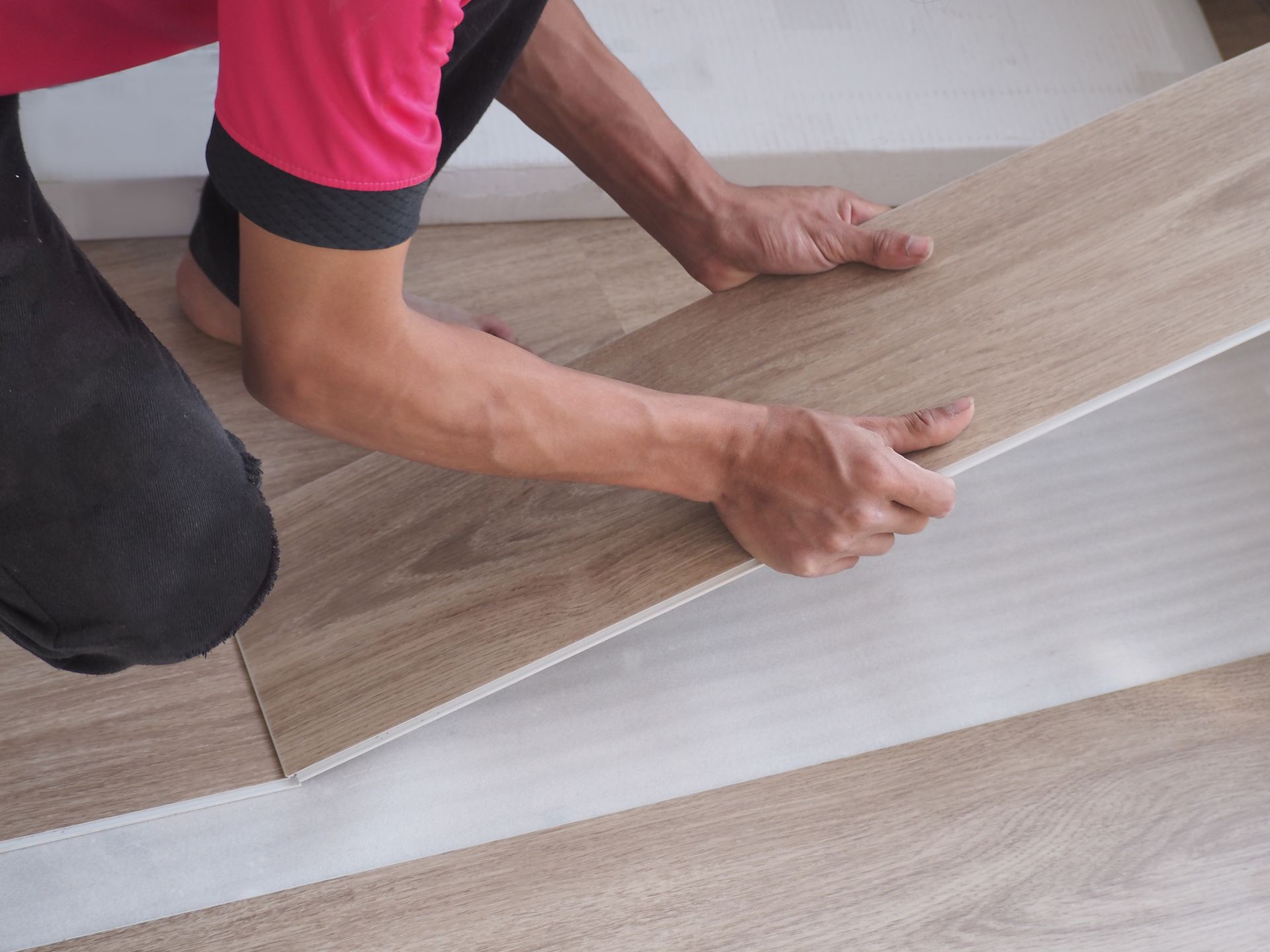 Person installing light wood floor plank in a room