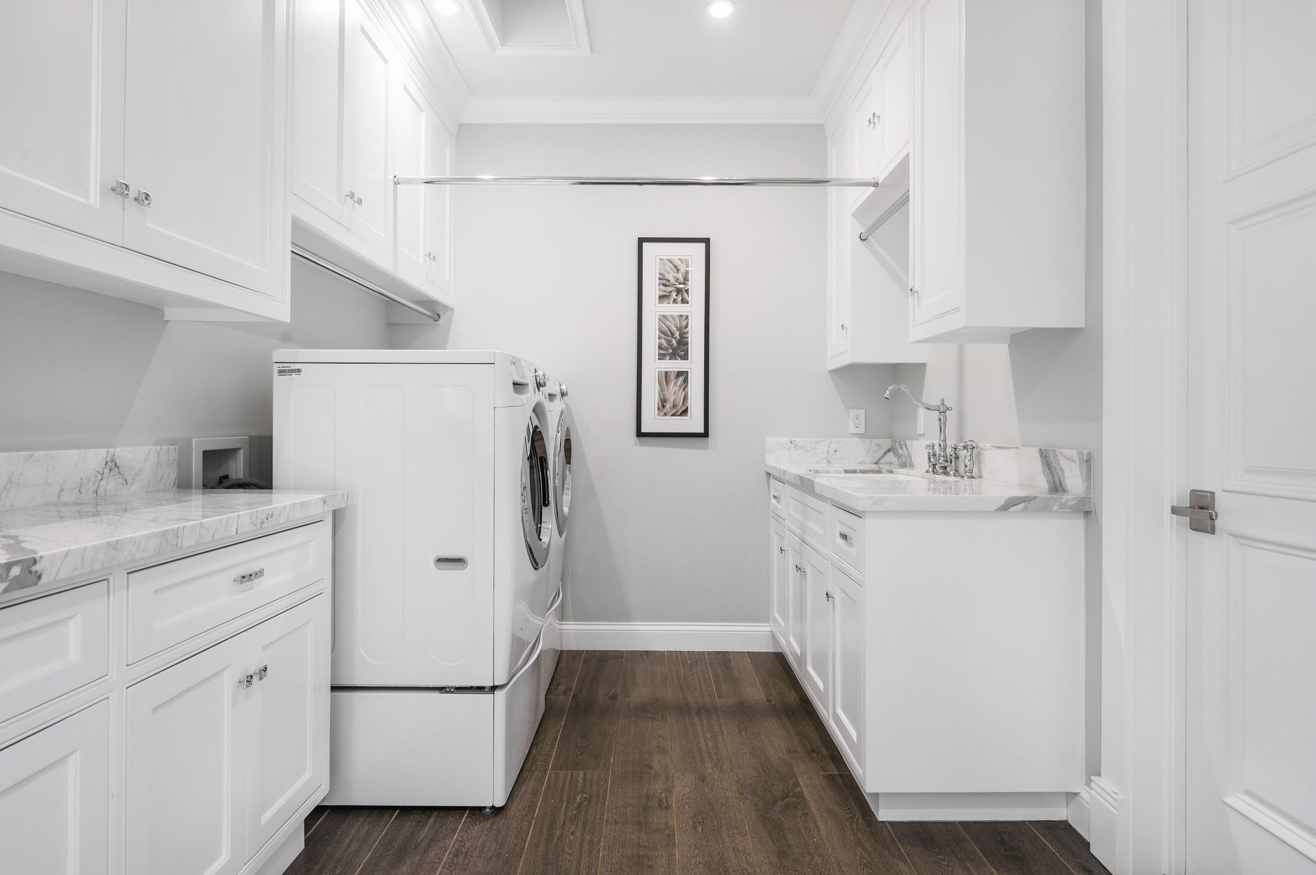 Bright white laundry room with washer, dryer, cabinets, and wood floor