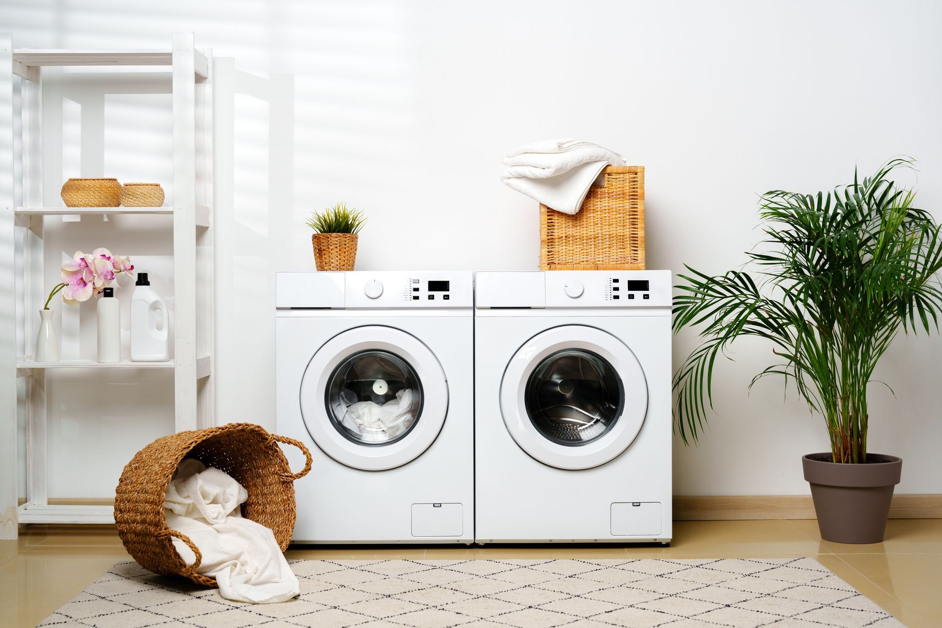 Bright laundry room with two front-loading washers, baskets, and a potted plant on a rug