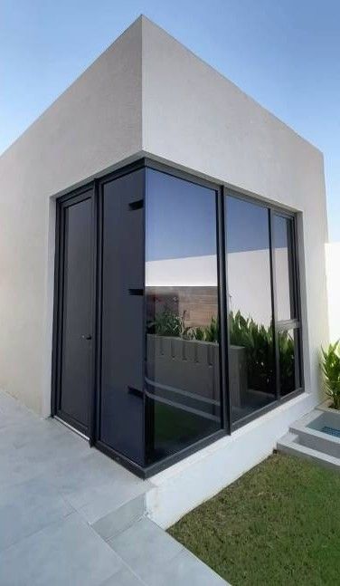 Rincón de una casa moderna blanca con grandes ventanales de cristal con marcos oscuros que reflejan el cielo y el jardín.