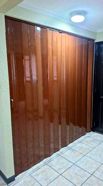 Puertas de armario de madera marrón brillante en un pasillo alicatado bajo una lámpara de techo.