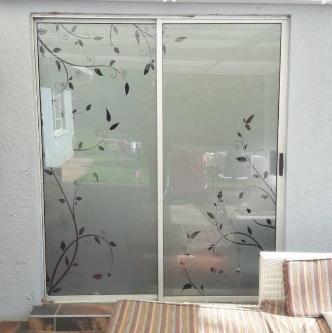 Puerta corrediza de vidrio con calcomanías florales esmeriladas y un pequeño banco al lado.