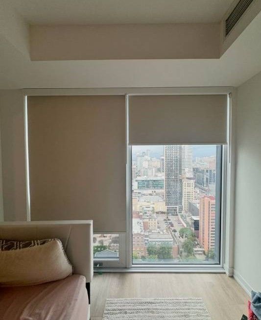 Dormitorio moderno de color beige con una cama bien hecha, lámparas de noche y una ventana con una persiana cerrada.