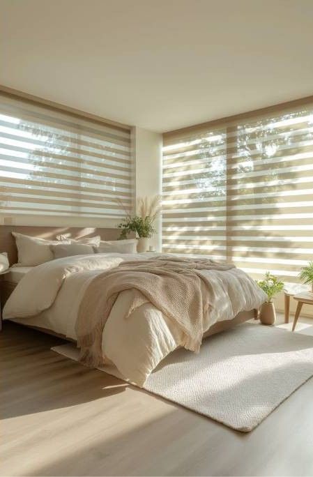 Dormitorio luminoso y minimalista con una cama beige, persianas a rayas y luz solar cálida en el suelo.