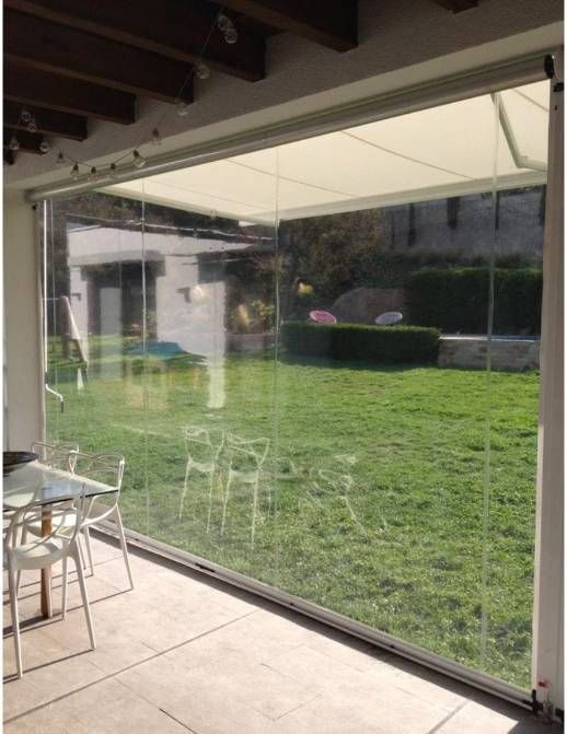 Patio con una gran pared de cristal transparente con vistas a un césped verde y un jardín bordeado de setos.