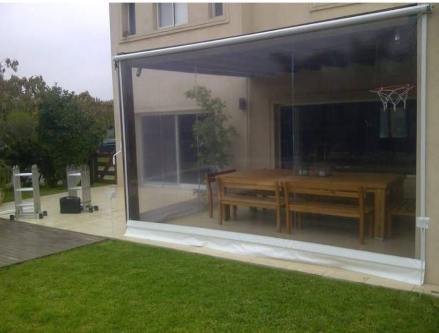 Patio con una gran pared de cristal transparente con vistas a un césped verde y un jardín bordeado de setos.