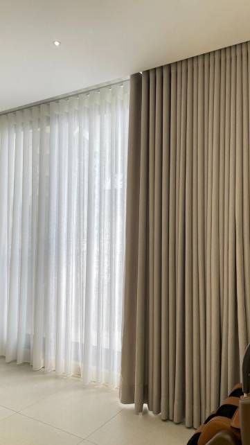 Habitación luminosa con cortinas altas de color beige, ventanas arqueadas y una alfombra blanca en el suelo.