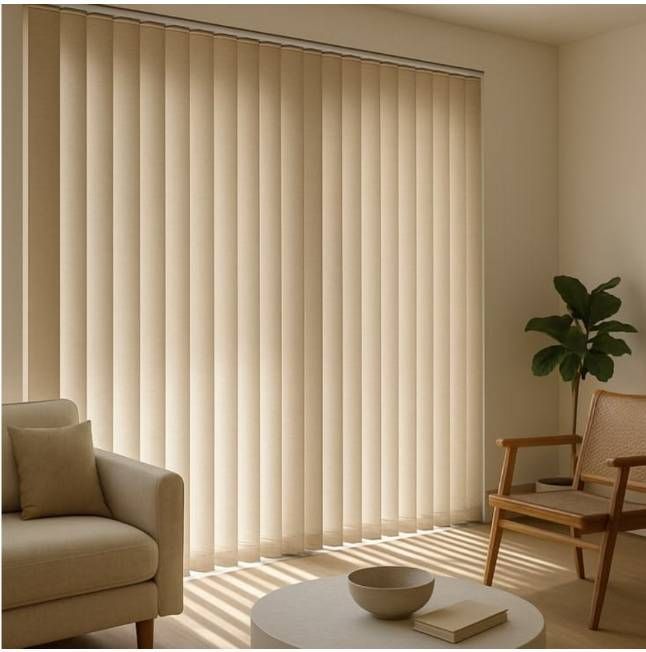 Sala de estar luminosa con persianas verticales beige, sofá, silla, planta y luz solar que proyecta sombras rayadas.
