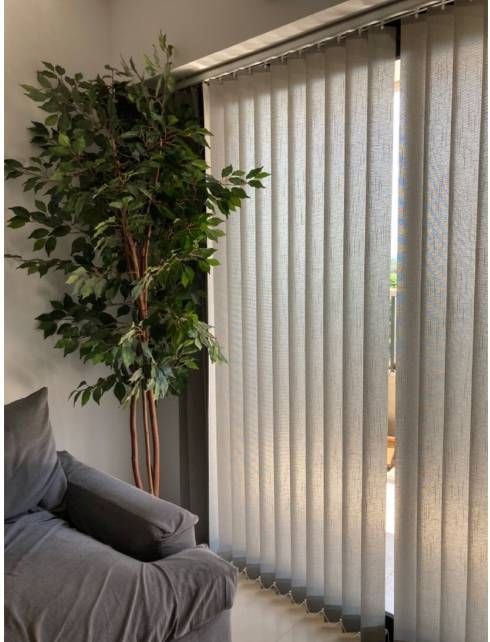 Persianas verticales beige cerradas que cubren una puerta de cristal en un pasillo blanco.